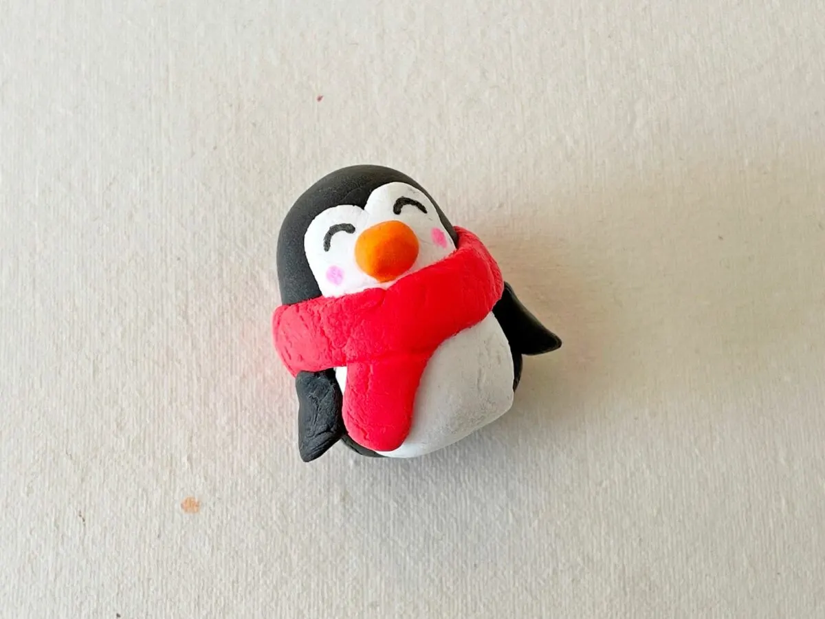 A penguin wearing a red scarf on a white surface.
