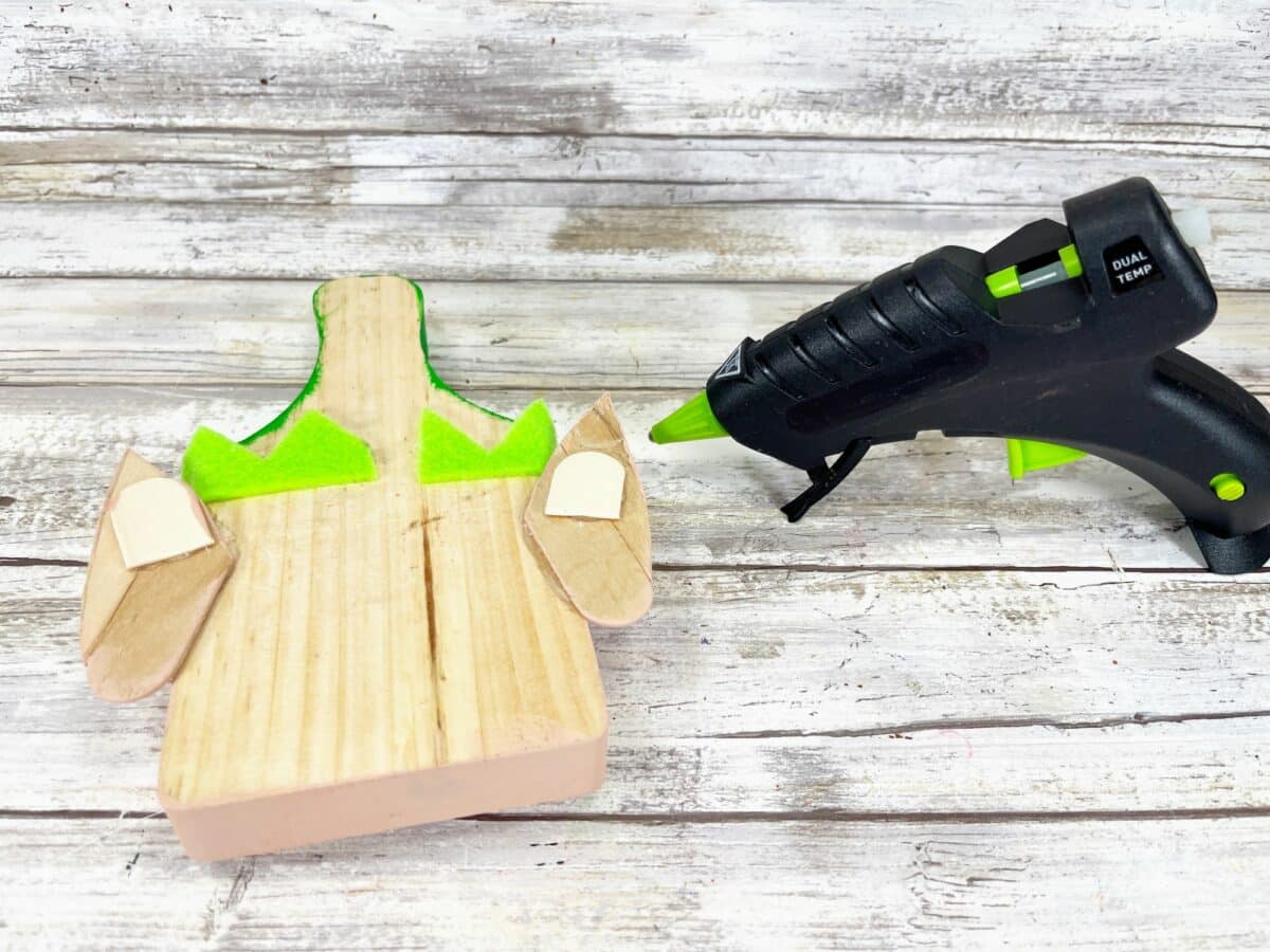 A green glue gun next to a wooden piece of wood.