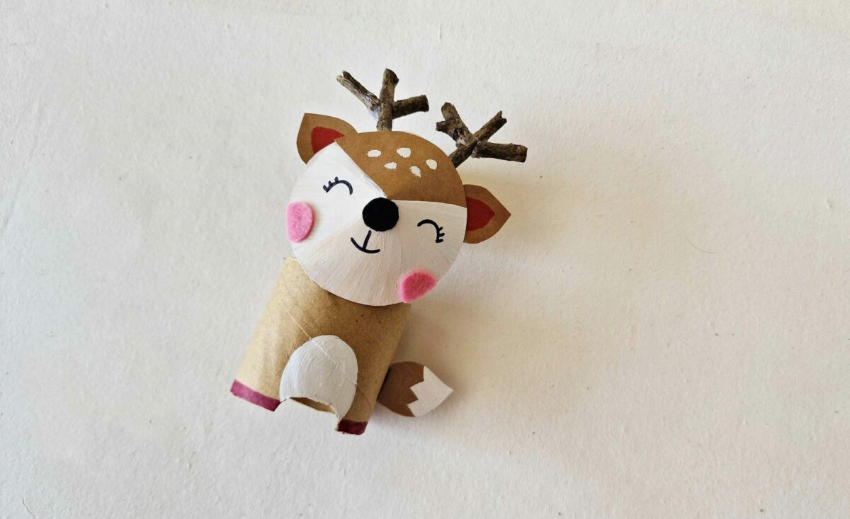 A wooden reindeer with a pink nose on a white surface.
