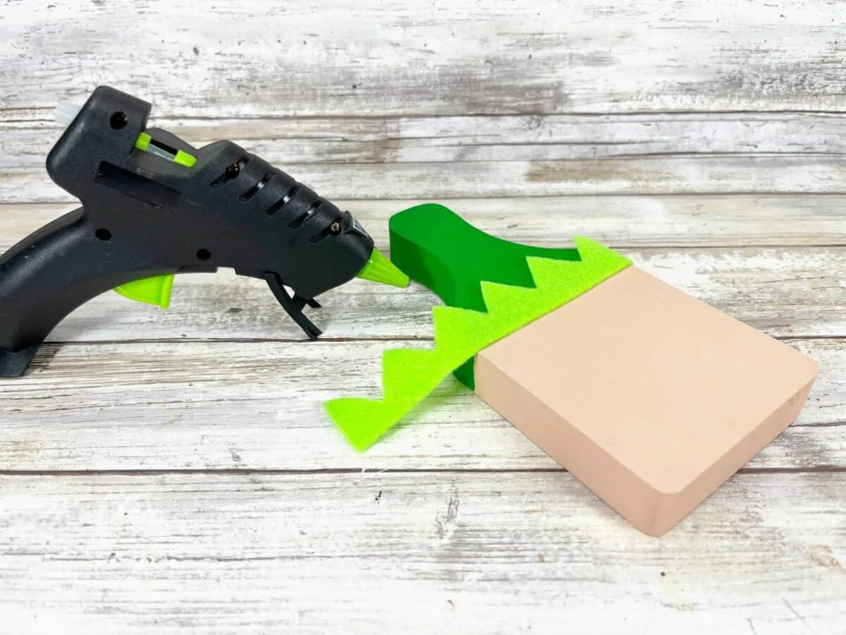 A green glue gun next to a wooden block.