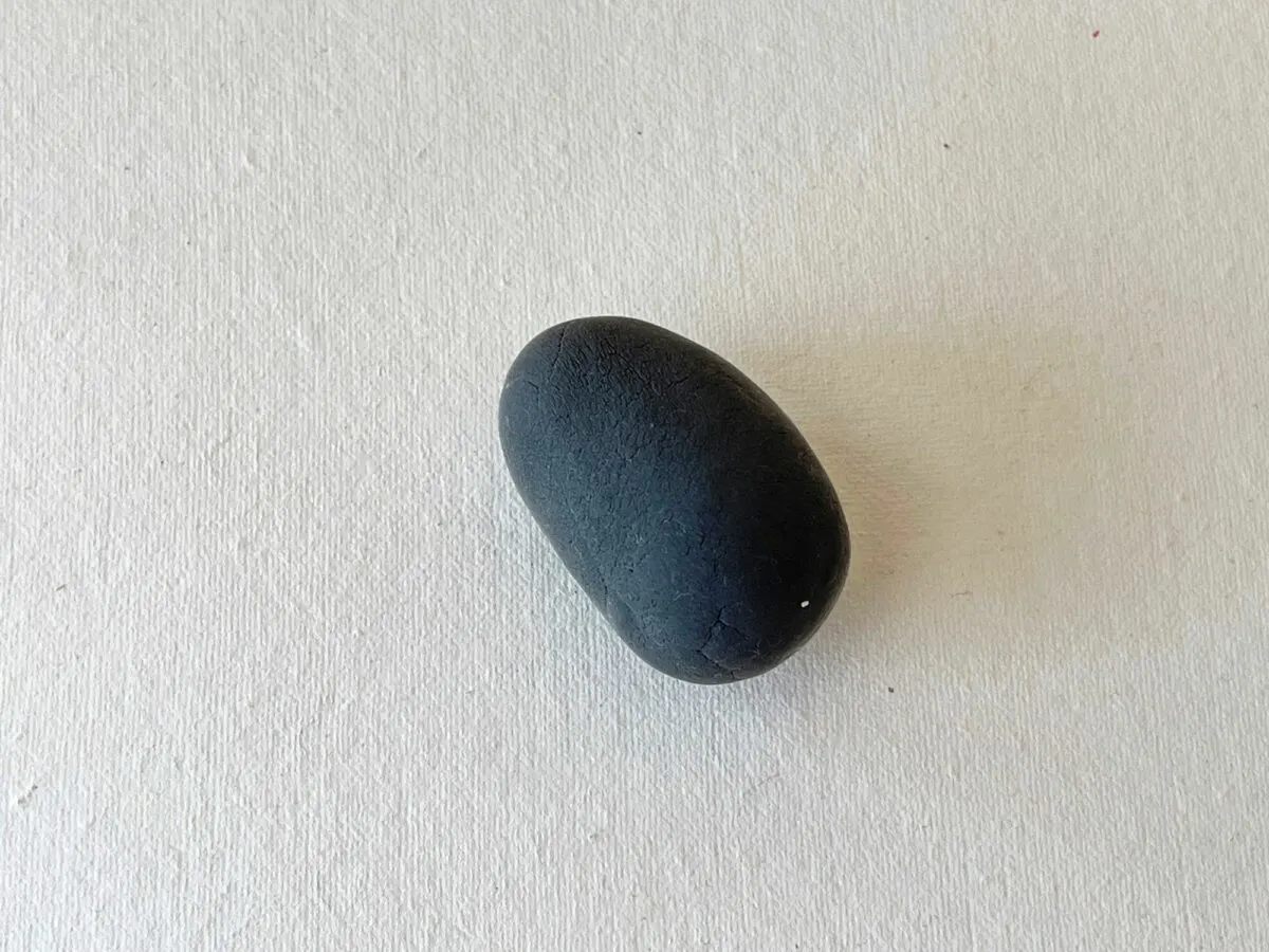 A small black rock sitting on a white surface.