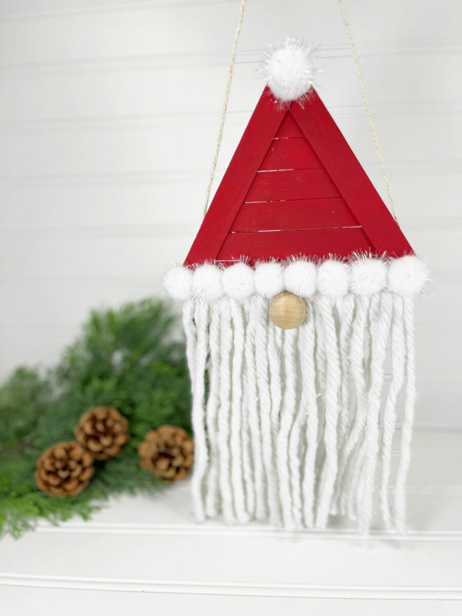 A santa claus hanging ornament with tassels and pine cones.