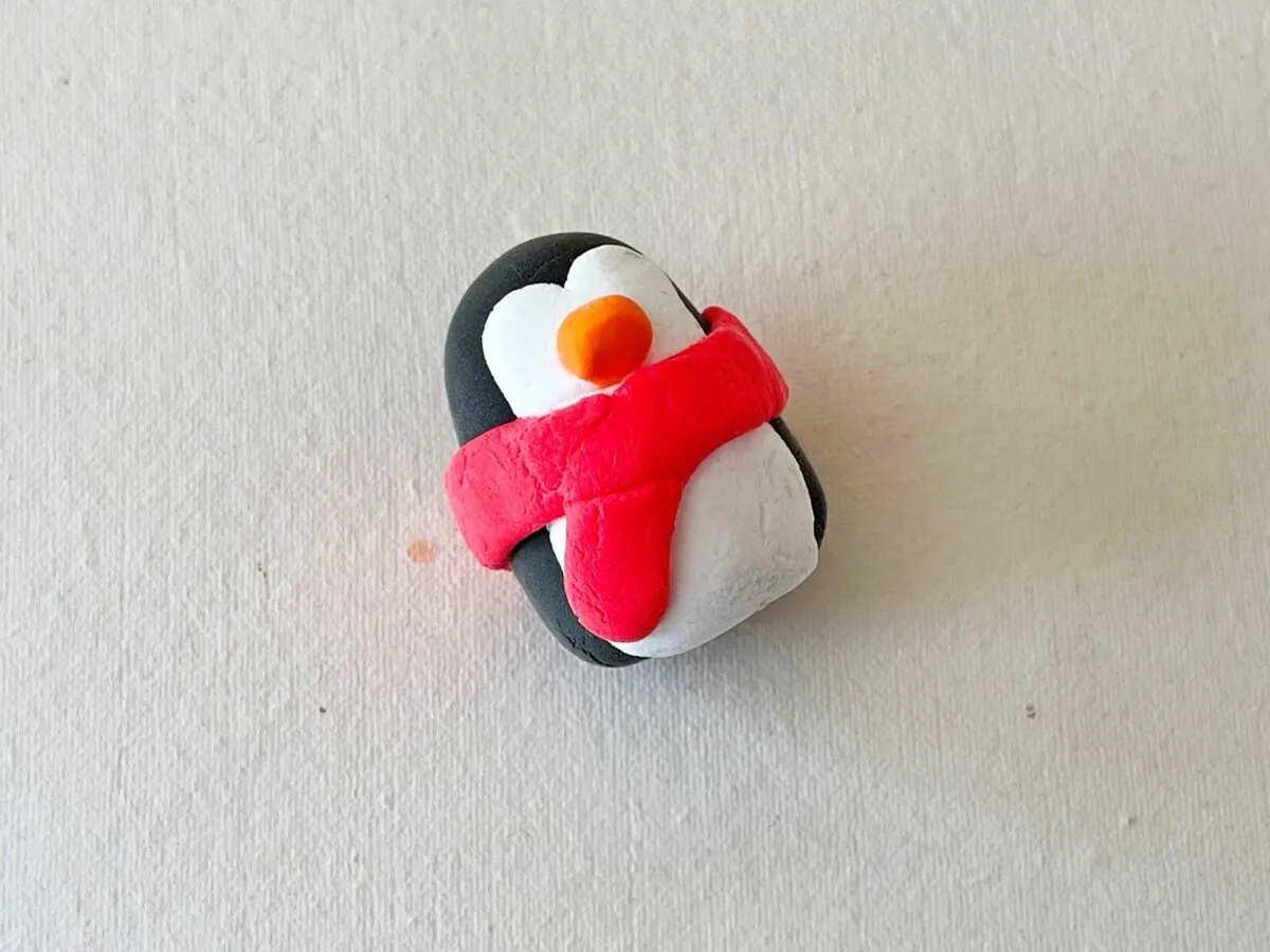A penguin with a red scarf on a white surface.