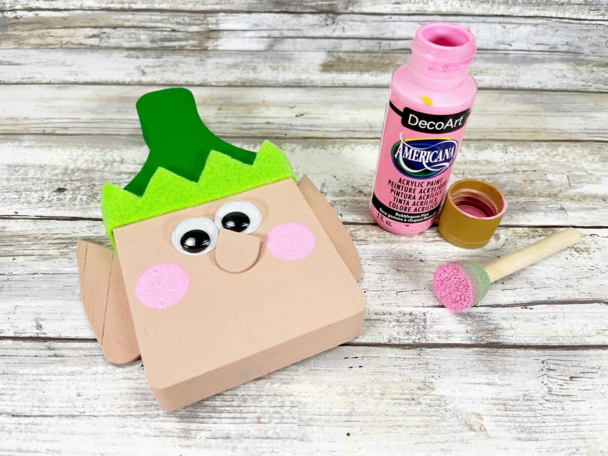 A wooden box with a paint brush and a bottle of pink paint.