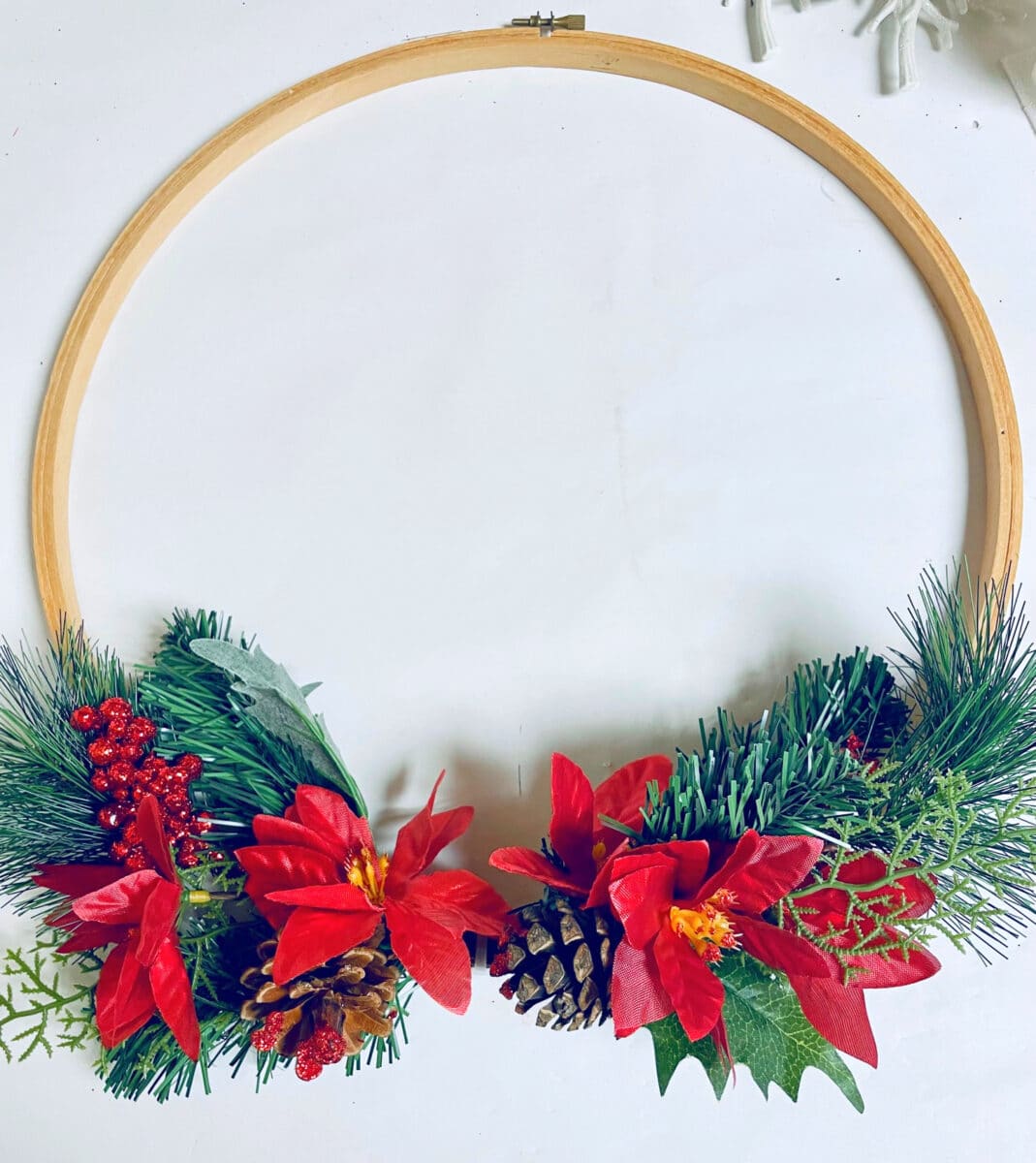 A wooden hoop with red poinsettias and pine cones.