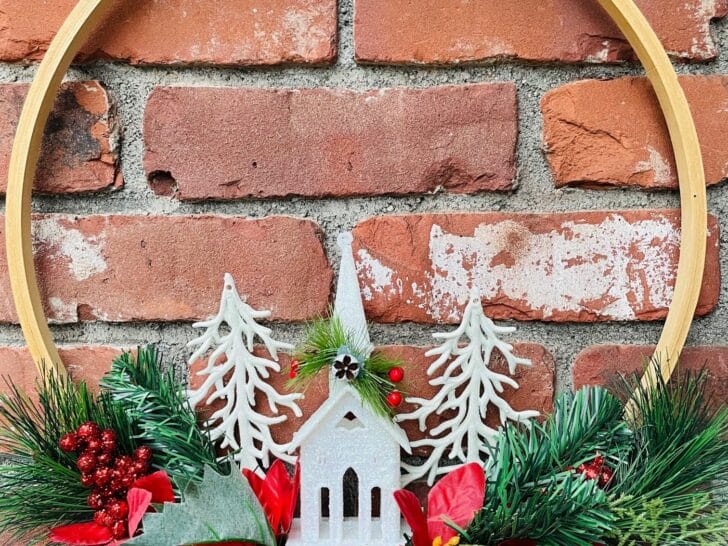 A christmas hoop wreath with a wooden church and pinecones.