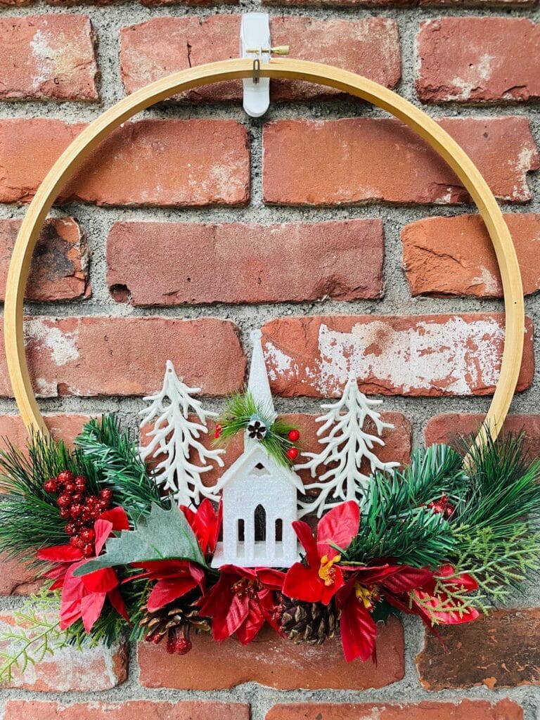 A christmas hoop wreath with a wooden church and pinecones.