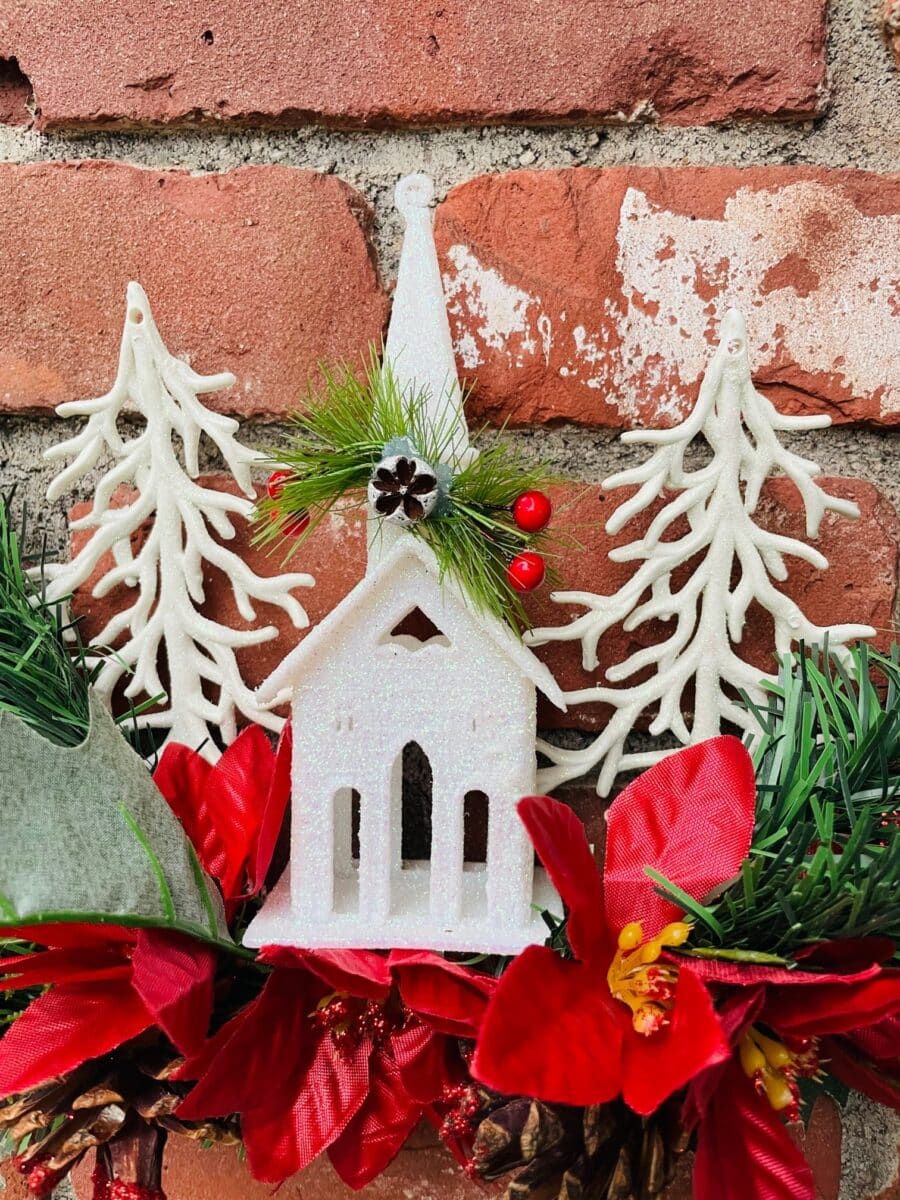 A christmas wreath with a white church and red poinsettias.