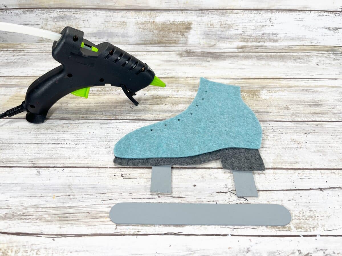 A pair of felt ice skates next to a glue gun.