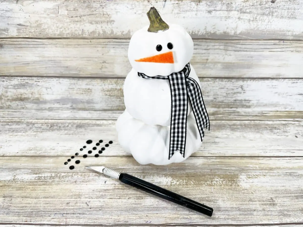 A snowman sitting on a wooden table next to a pen.