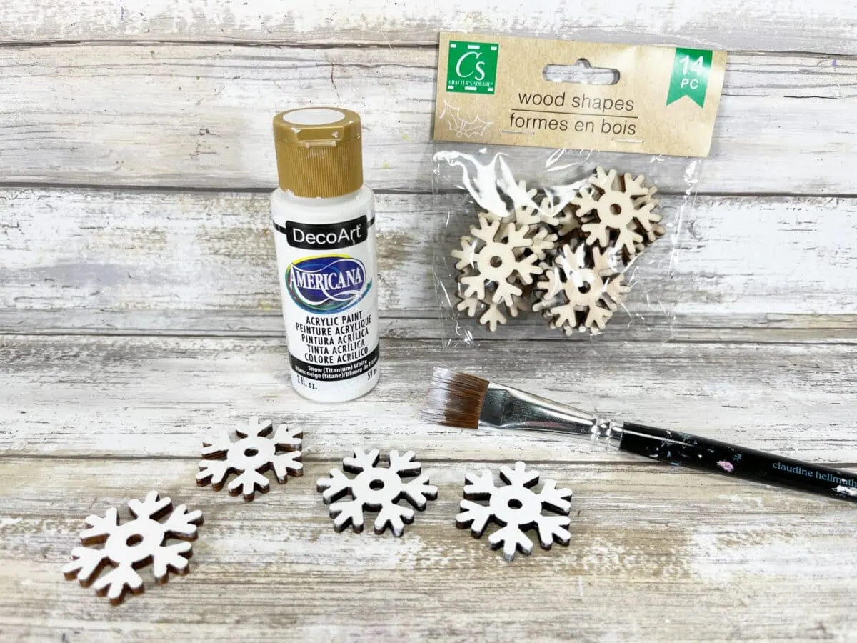 Snowflake ornaments and a paint brush on a wooden table.