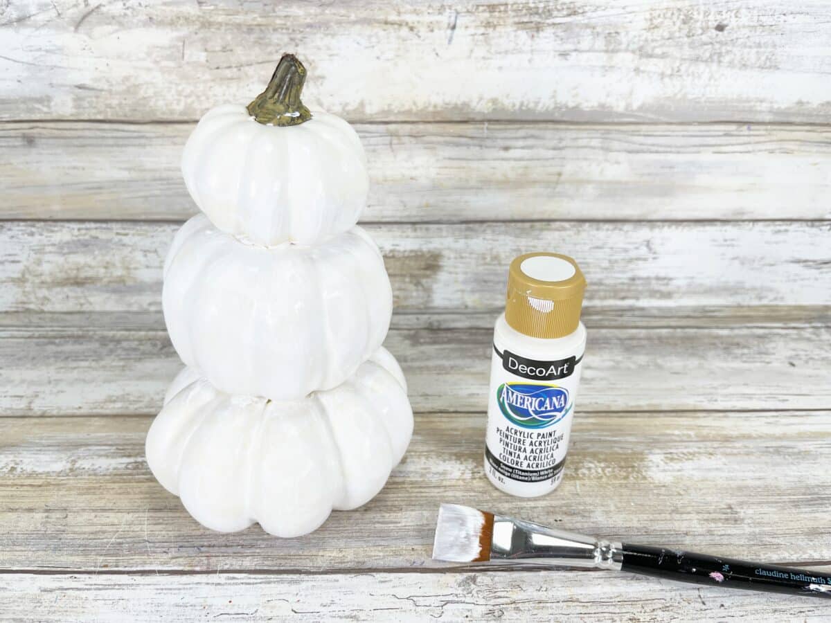 A white pumpkin on a wooden table next to a paint brush.
