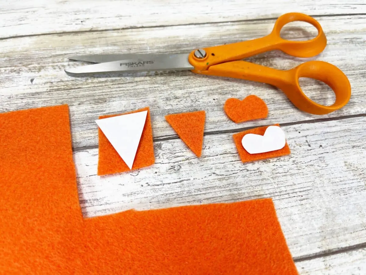 A pair of scissors and orange felt pieces on a table.