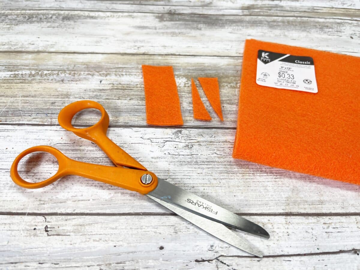 A pair of orange scissors next to a piece of felt.