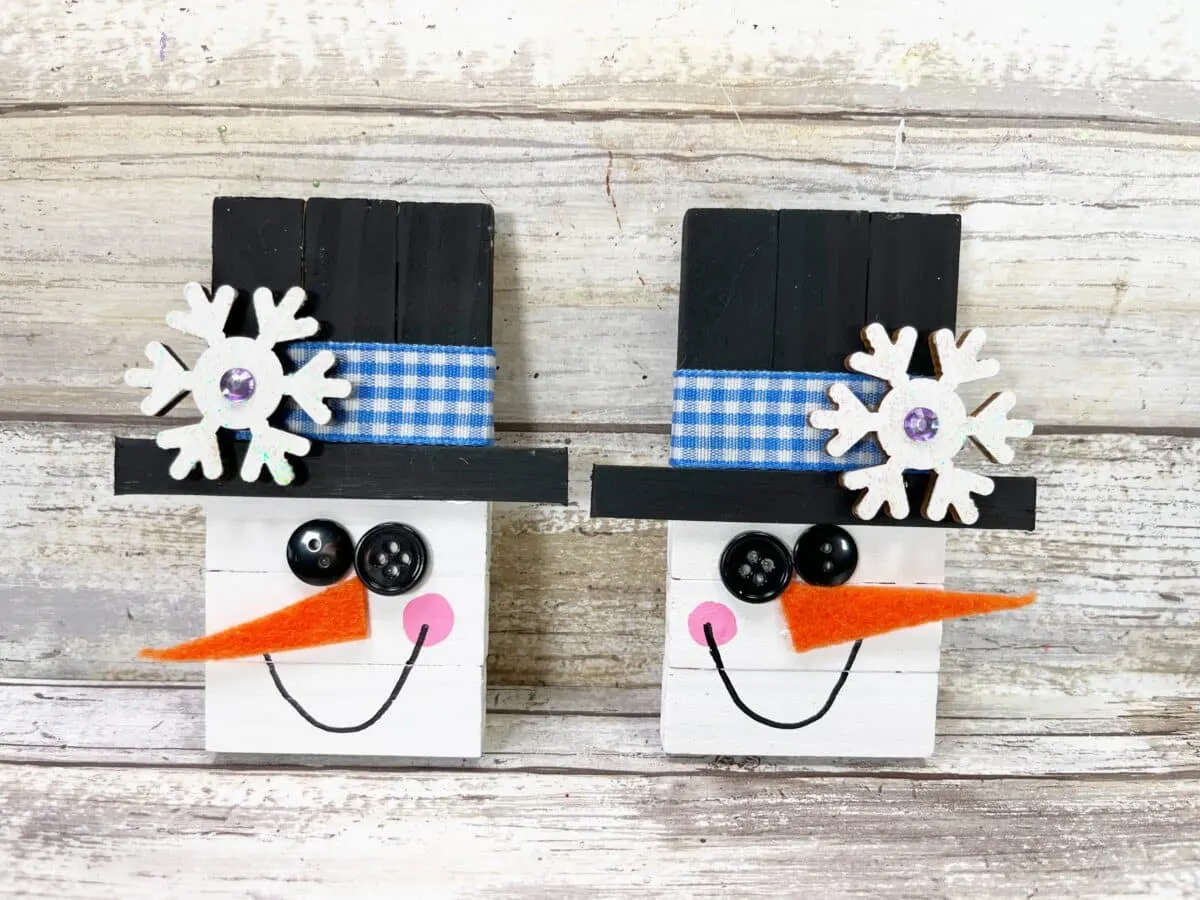 Two wooden snowmen with hats and snowflakes on them.