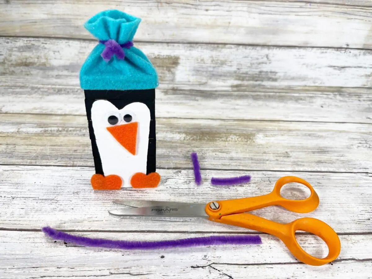 A felt penguin craft with scissors and a felt penguin hat.
