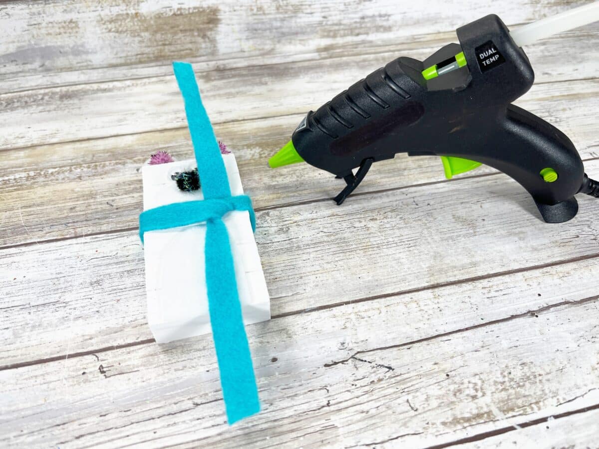 A glue gun with a blue ribbon next to it.