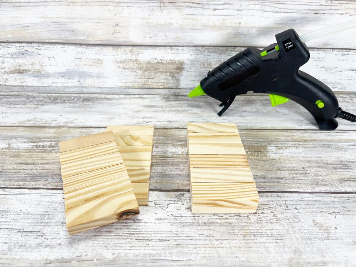 A glue gun and wood pieces on a wooden table.