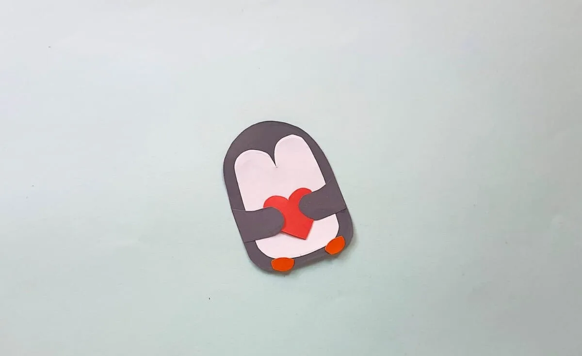 Penguin Bookmark Step 7 A penguin holding a heart on a white surface.