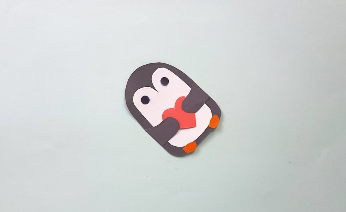 Penguin Bookmark Step 8 A penguin holding a heart on a white surface.