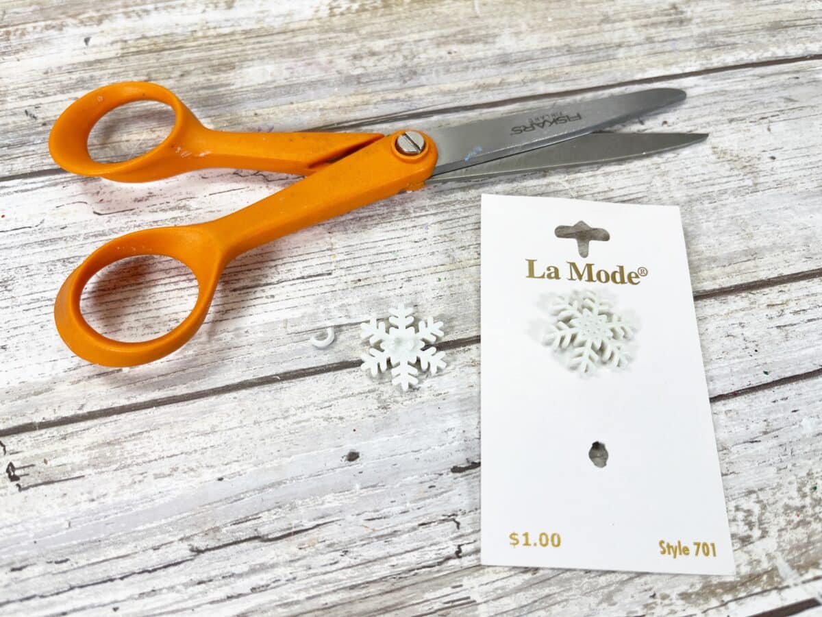 A pair of orange scissors next to a package of snowflakes.