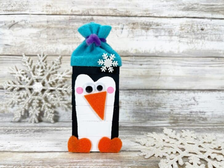 A felt penguin bottle holder with snowflakes on it.