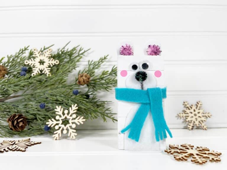 A felt polar bear with a scarf and pinecones.