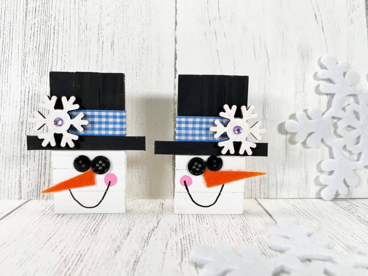 Two wooden snowmen with hats and snowflakes on them.