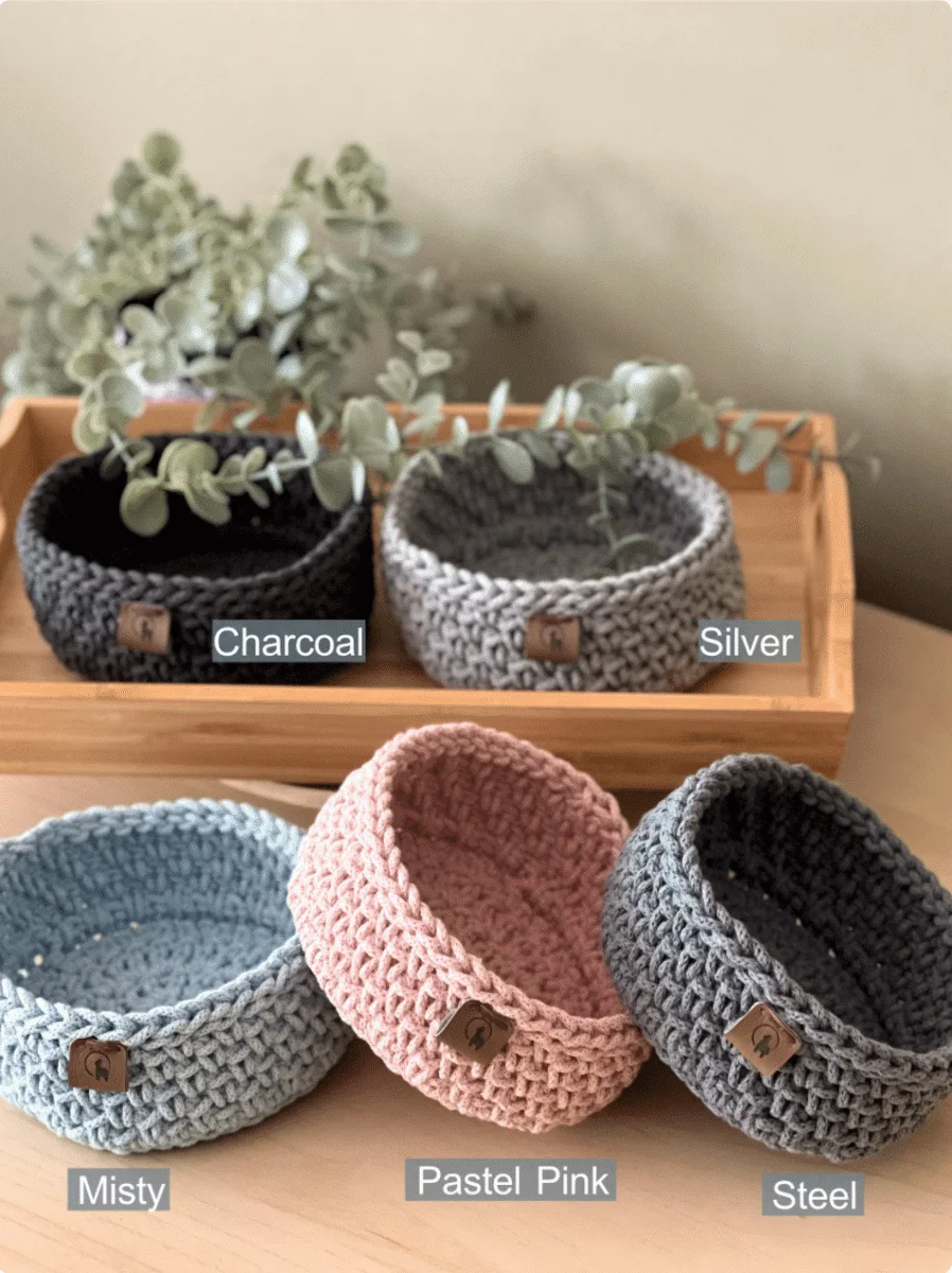 Four crocheted bowls displayed on a wooden table, perfect for a beginner crochet kit.