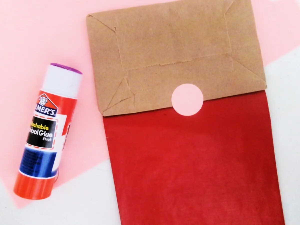 A red paper bag with a glue stick next to it, resembling a Santa gnome handprint.