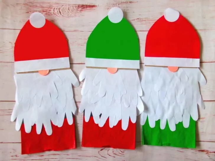 Three santa claus paper crafts on a wooden table.