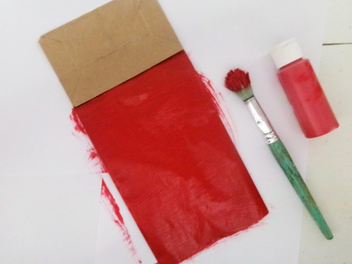 A red paintbrush rests next to a paper bag.