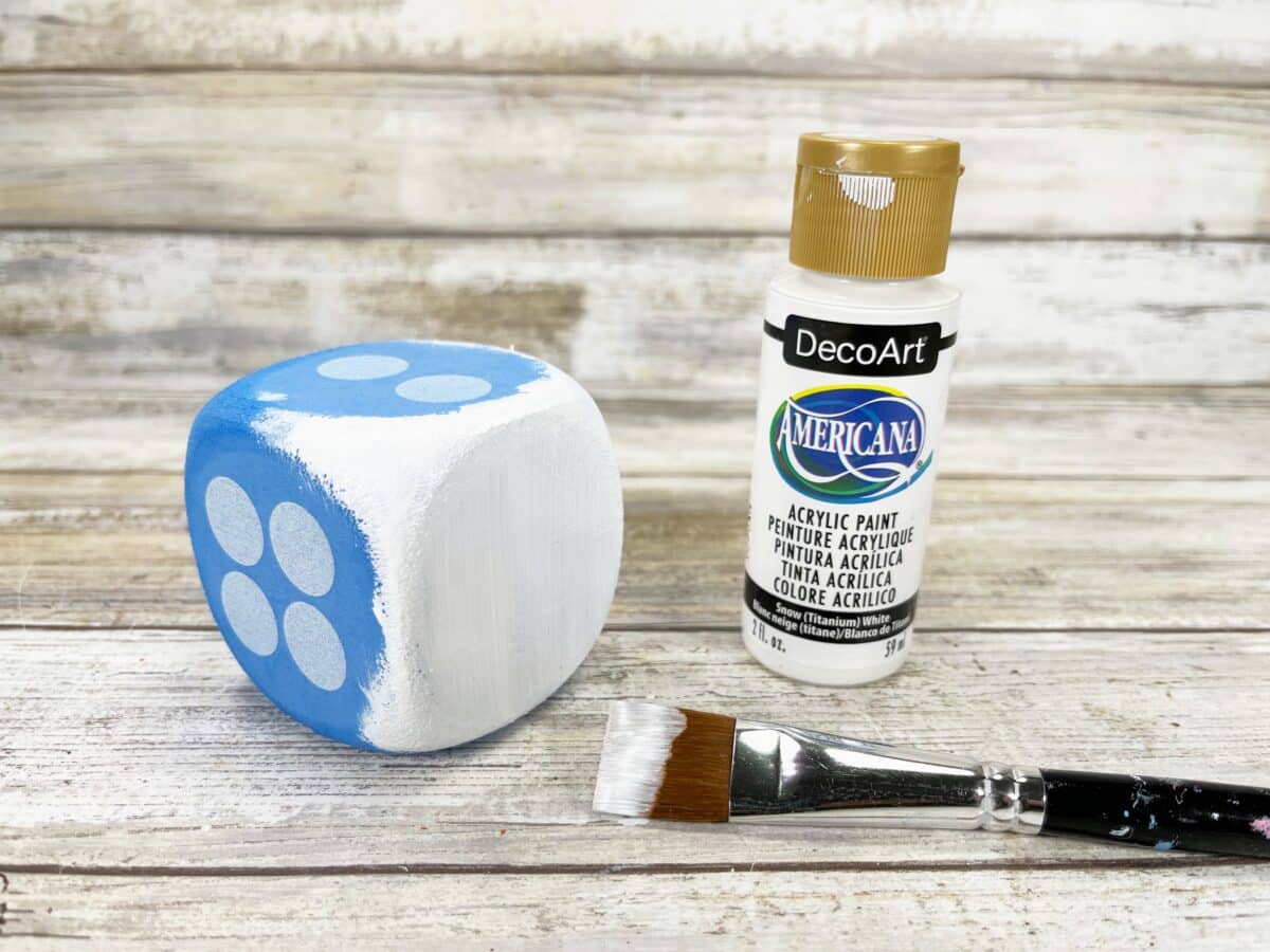 A blue and white painted dice next to a paint brush.