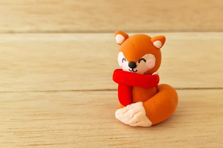 A small clay fox figurine wearing a scarf.