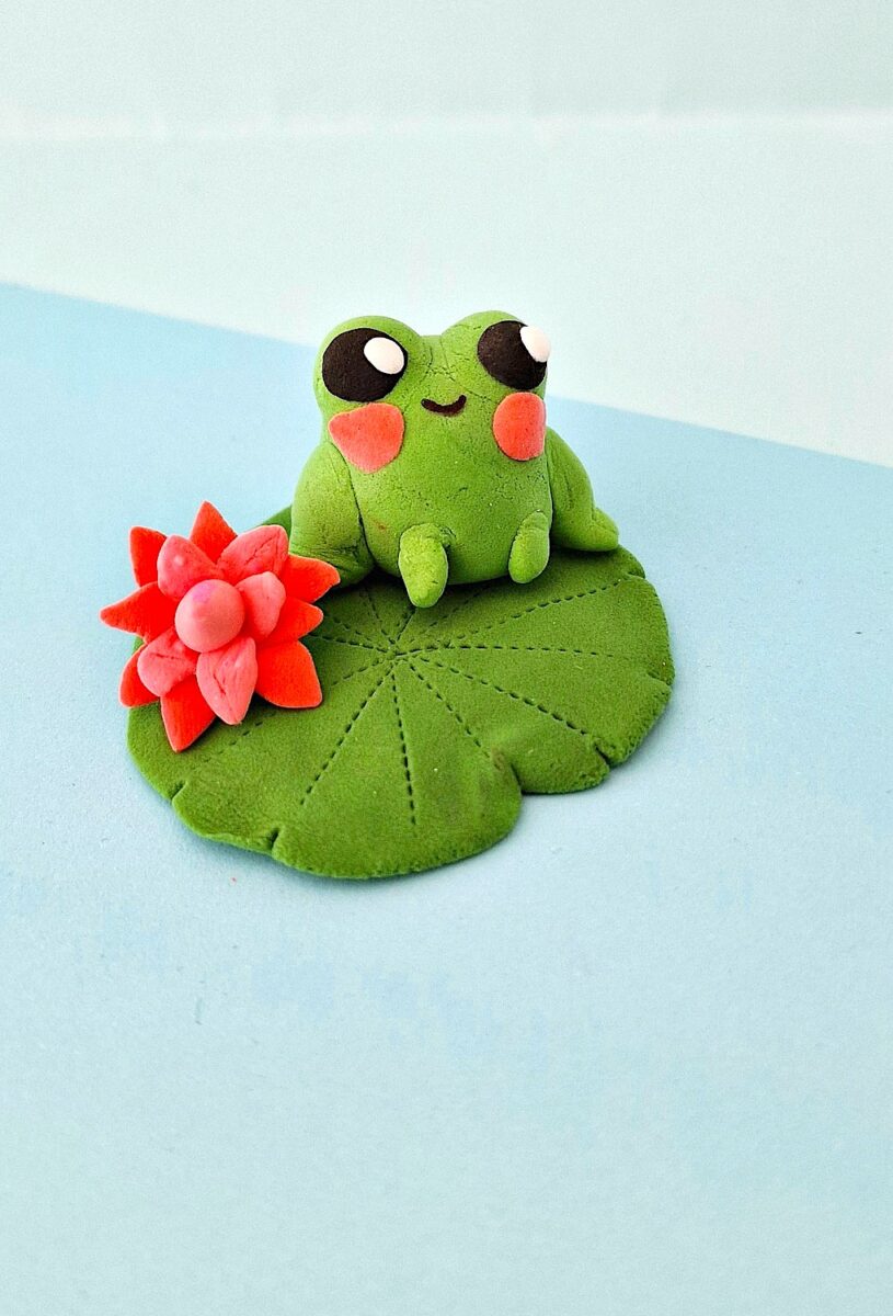 Clay Frog with an orange clay flower and lily pad on a blue background