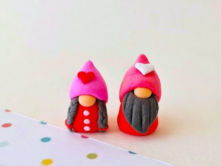 A pair of clay gnomes in pink and red sitting on top of a polka dot background.
