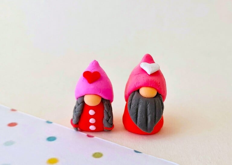 A pair of clay gnomes in pink and red sitting on top of a polka dot background.