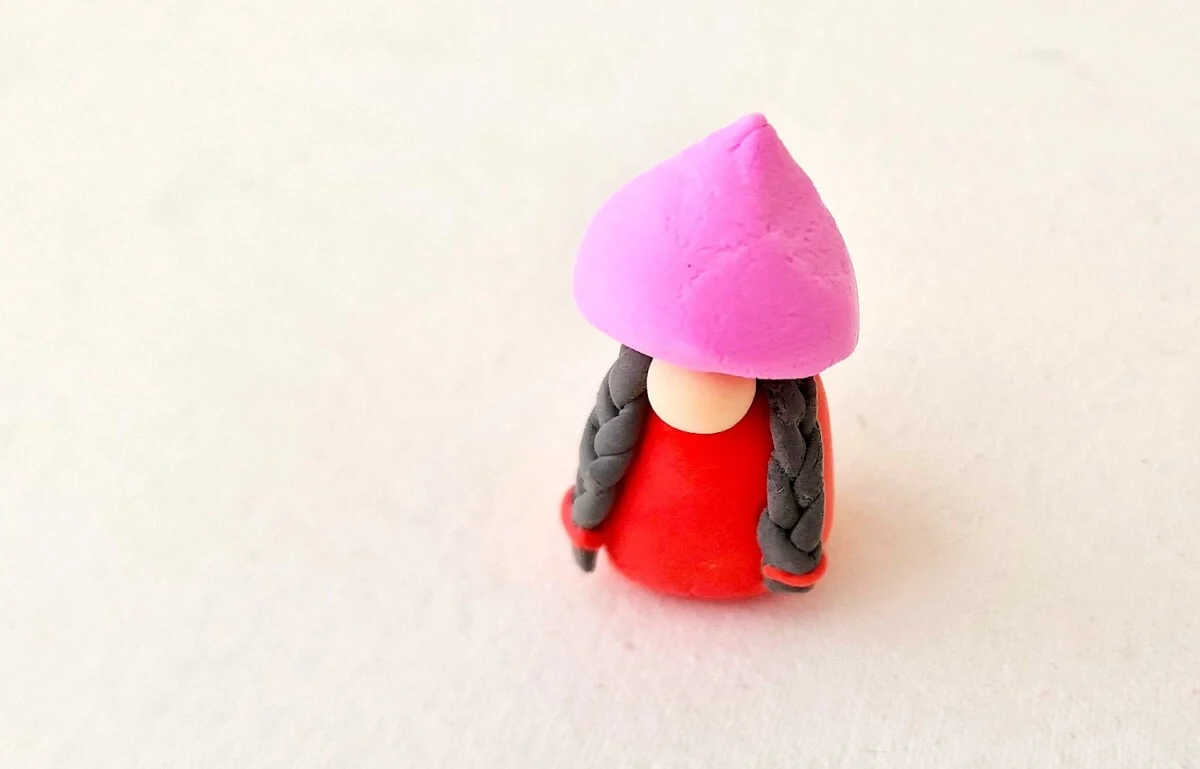 Clay Gnome Step 14 A small figurine with a pink hat on a white surface.