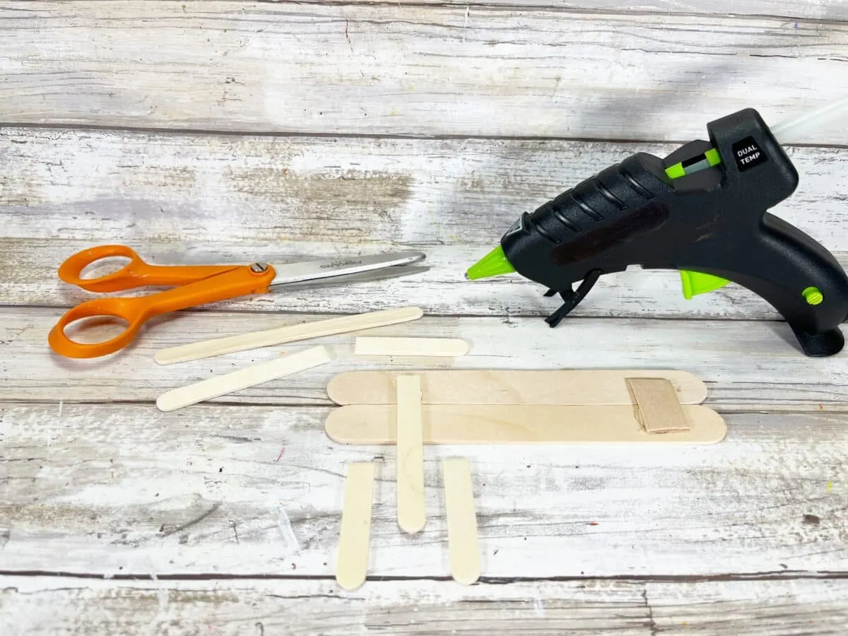 A glue gun, scissors and glue sticks on a wooden table.