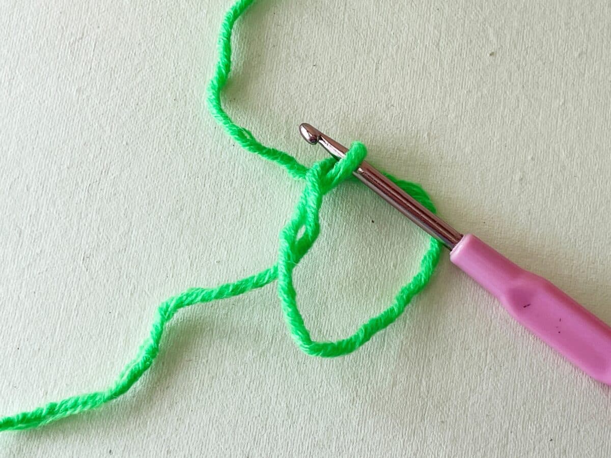 A pink crochet hook with a green yarn.