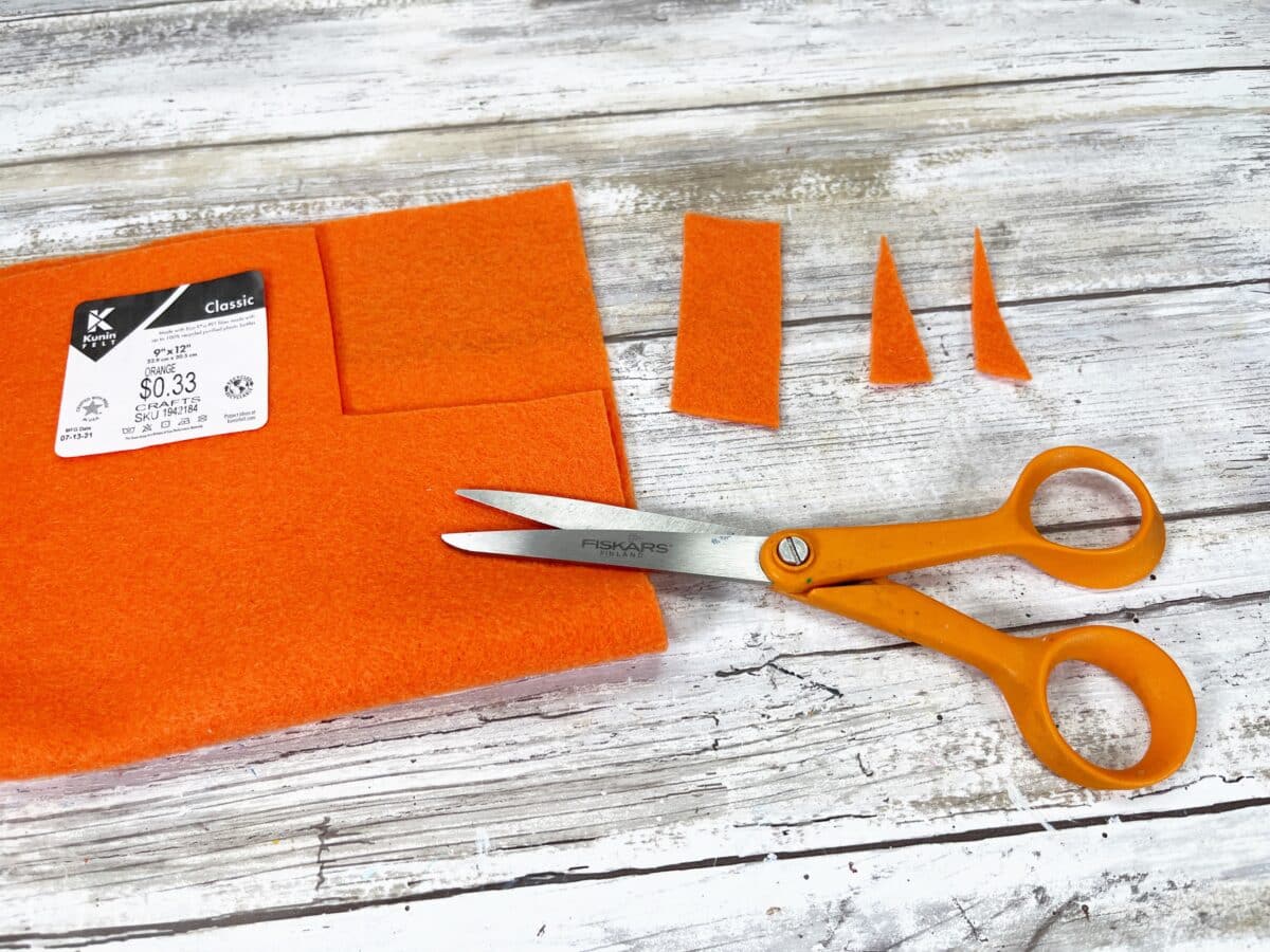 A pair of scissors and an orange felt bag on a wooden table.