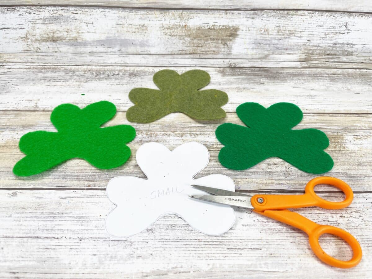 Shamrock felt leaves and scissors on a wooden table.