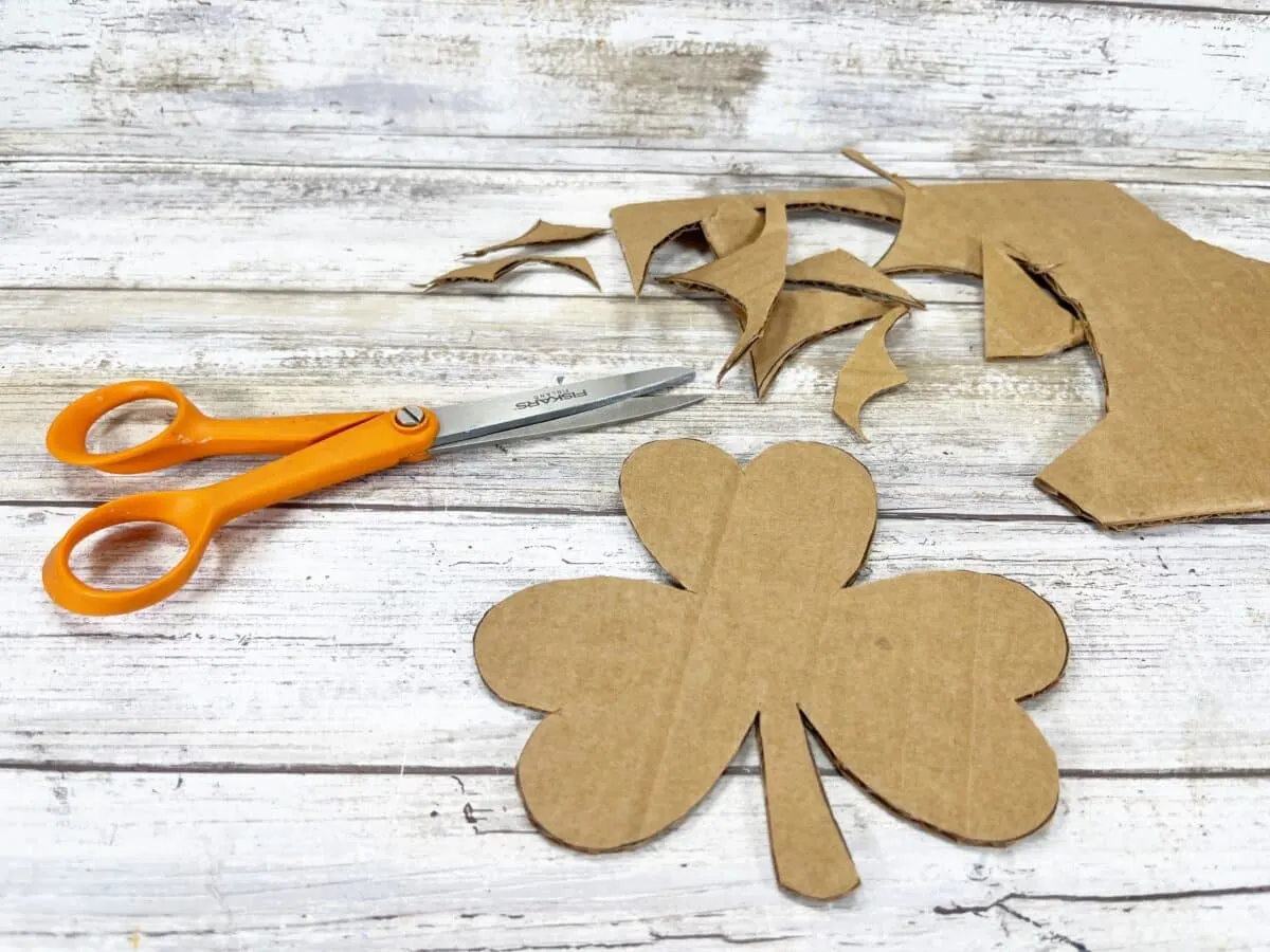 A pair of scissors next to a cardboard shamrock.