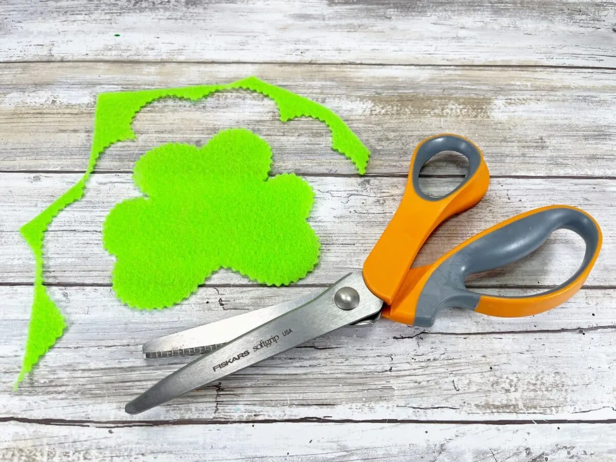 A pair of scissors next to a green felt shamrock.
