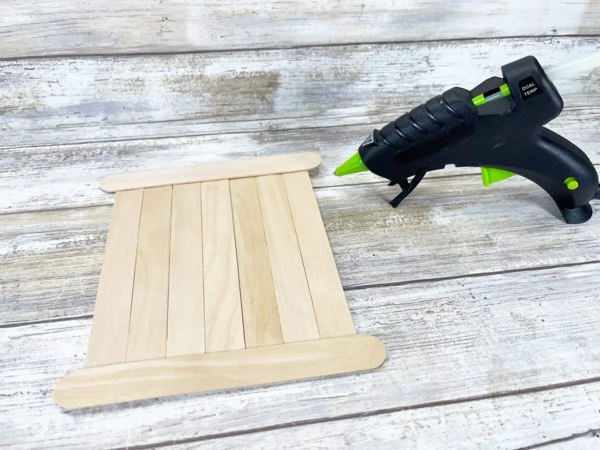 A glue gun next to a wooden plank.