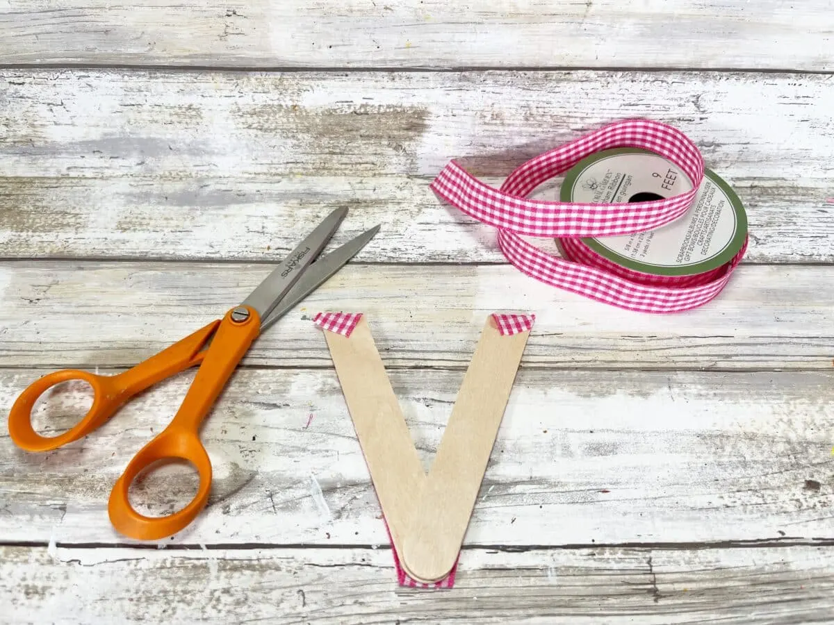 A pair of scissors and a pink ribbon on a wooden table.