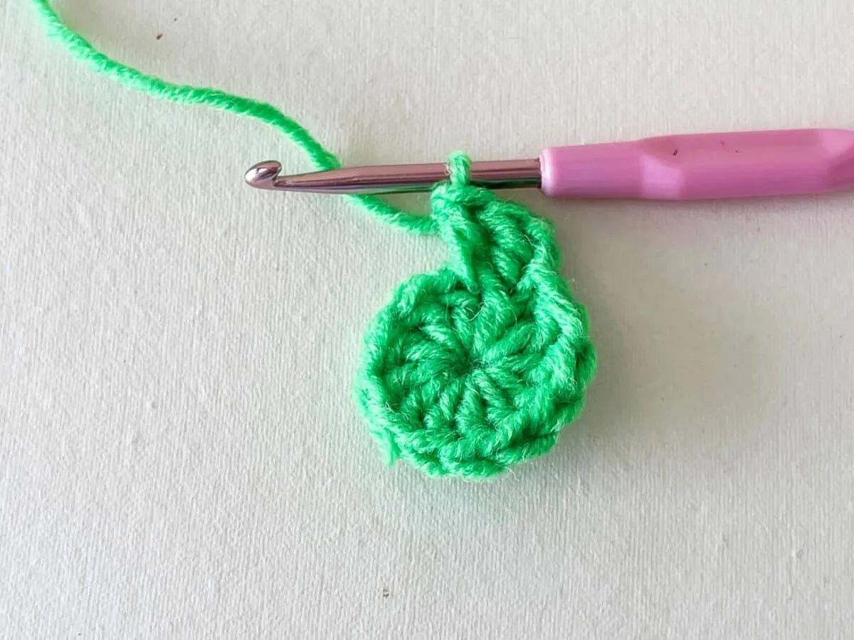A green crocheted flower with a pink crochet hook.