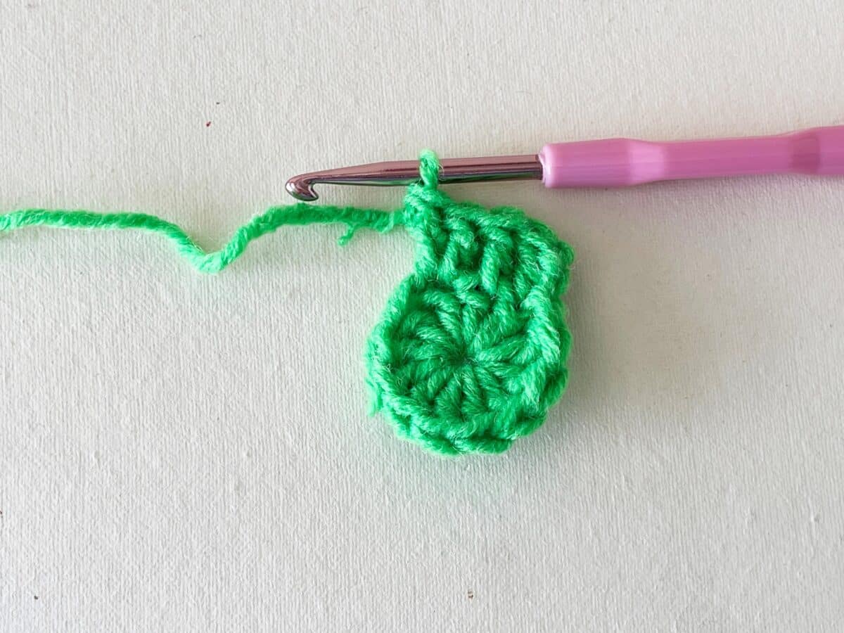A green crocheted ball with a pink crochet hook.
