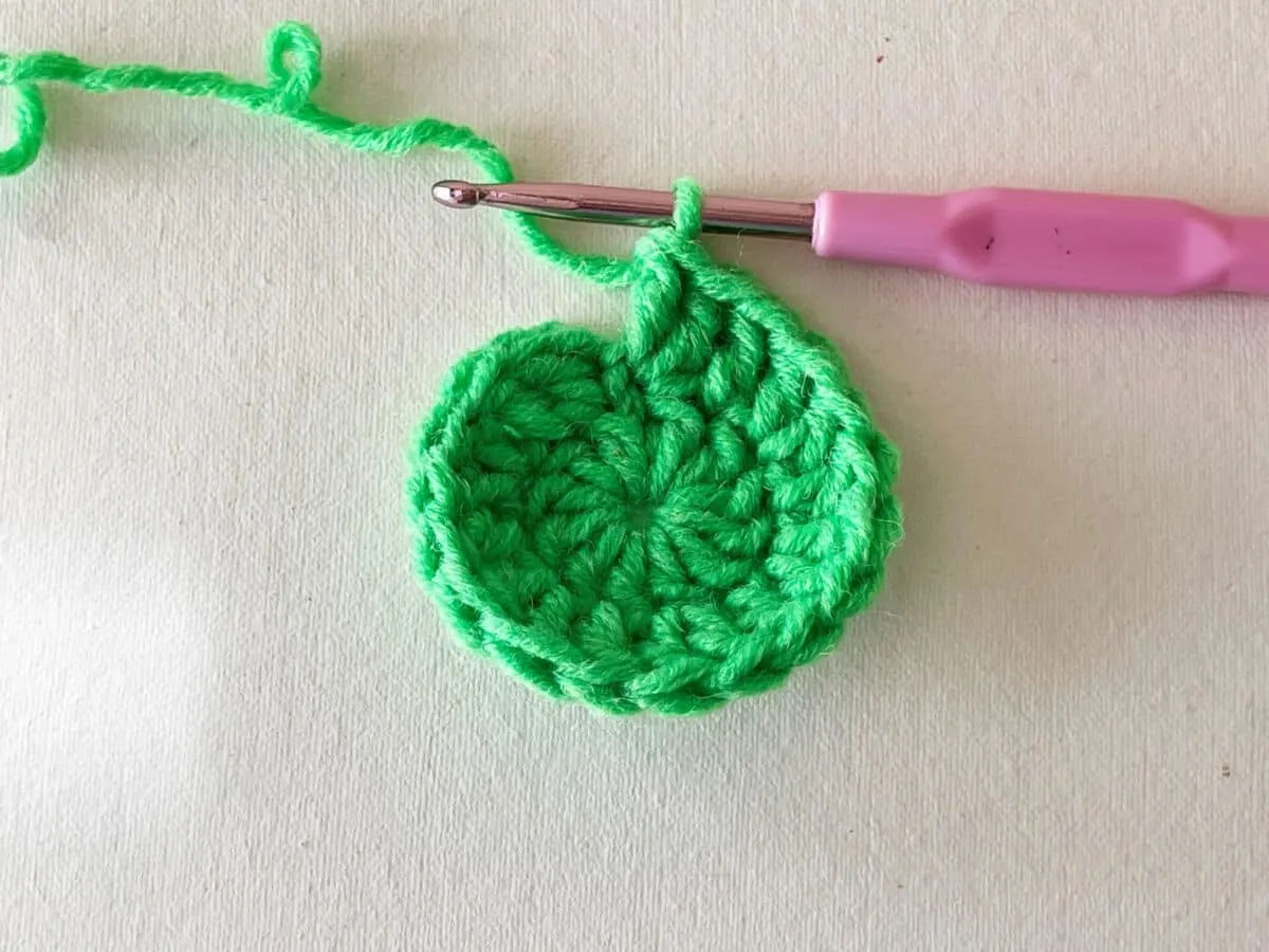 A green crocheted leaf with a pink crochet hook.