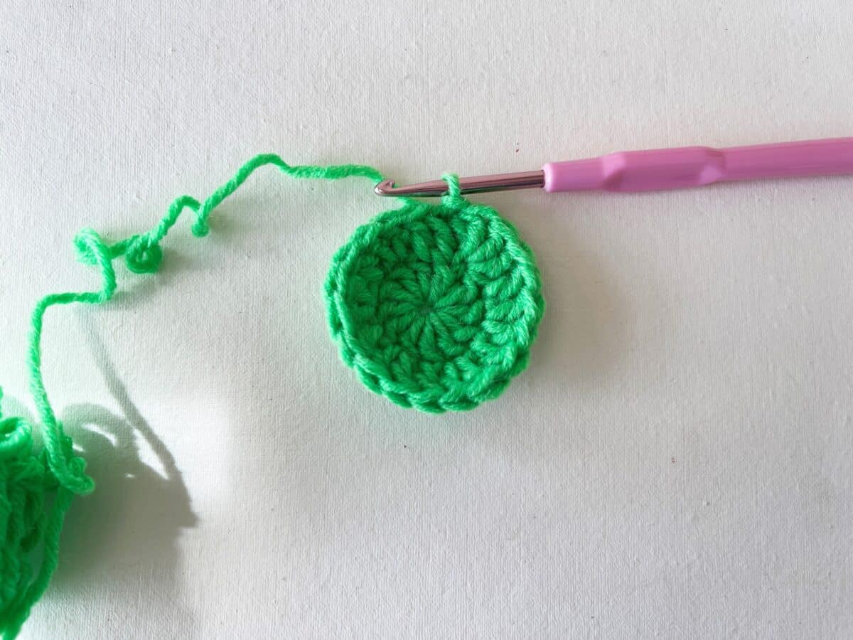 A green crocheted ball with a pink crochet hook.